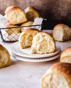 several rolls on plates next to a basket with one half eaten and the other half empty