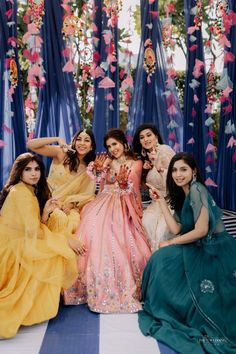 four women pose for a photo in front of blue drapes and hanging flower garlands