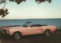 an old pink convertible car parked by the water