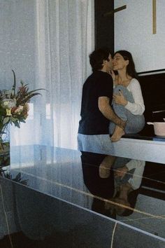 a man and woman kissing in front of a piano with their reflection on the floor