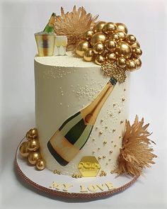 a white cake decorated with gold decorations and a bottle of champagne on the top tier