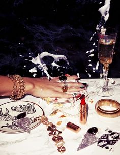 a table topped with lots of jewelry next to a glass filled with liquid and confetti