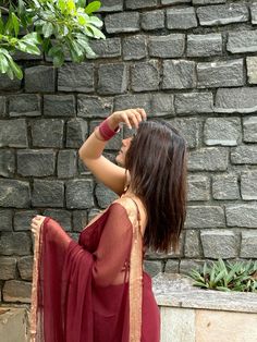 a woman in a red sari standing next to a brick wall