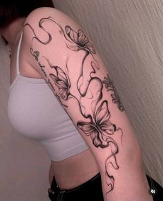 a woman's arm with flowers and butterflies tattoo on her left arm, behind her is a white tank top