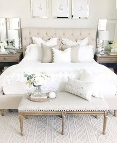 a white bed sitting next to two tables with flowers on top of it and pictures above the bed