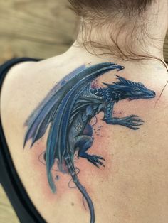 the back of a woman's shoulder with a blue dragon tattoo on her upper arm