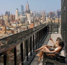 a woman sitting on top of a balcony next to a tall building holding a drink