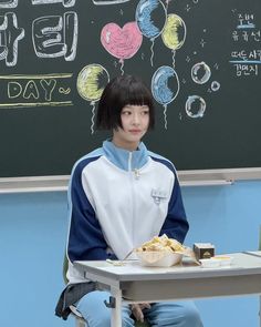 a boy sitting at a table with food in front of him and balloons on the chalkboard behind him