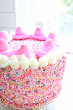 a pink cake with white frosting and sprinkles sitting on a table