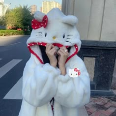 a person in a hello kitty costume on the street with her hands under her face