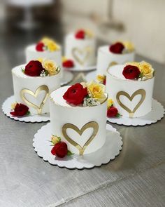 four white cakes with gold hearts and roses on each one are sitting on a table