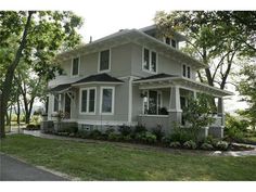 a gray house sitting on the side of a road next to trees and grass in front of it