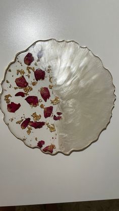 a white and gold plate with red flowers on the rim, sitting on a table