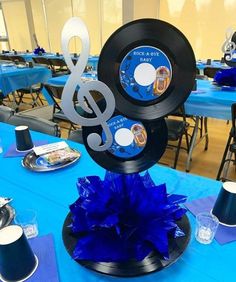 there is a music themed centerpiece on top of a blue table cloth with black and white decorations