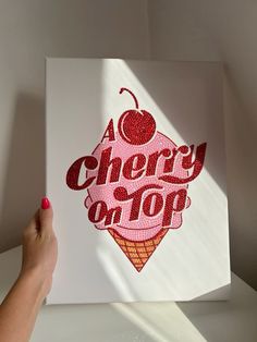 a person holding up a piece of art with the words cherry on top in red