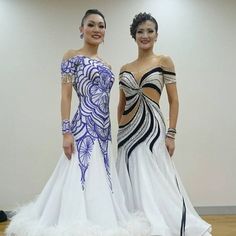 two women standing next to each other on a wooden floor wearing dresses with feather trims