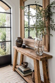 a wooden table topped with a vase filled with flowers next to a mirror and window