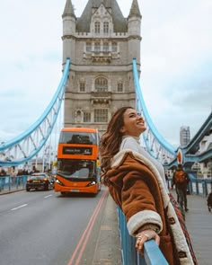 a woman standing on the side of a bridge next to a red double decker bus