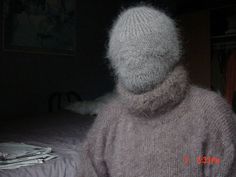 a person wearing a hat and sweater standing in front of a bed