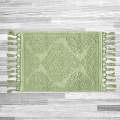 a green rug with tassels on top of a wooden floor next to a white wall