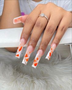 a woman's hand with orange and white nail designs on her nails, sitting on a chair