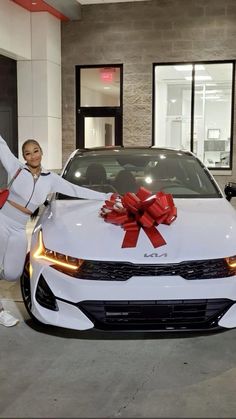 a woman standing next to a white car with a red bow on it