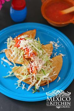 two tortilla shells with shredded cheese and tomato sauce on a blue plate next to an orange bowl