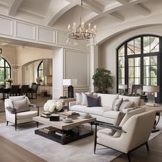 a living room filled with furniture and a chandelier hanging from the ceiling in front of large windows