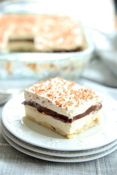 two desserts are sitting on white plates with silverware in the background and one has a slice missing from it