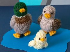 three knitted birds sitting next to each other on a blue tablecloth with a green hat