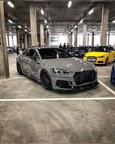 several cars are parked in an empty parking garage with people standing around them and looking at them