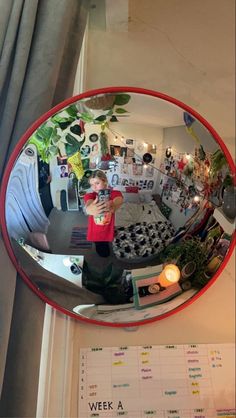 a young boy is taking a selfie in the reflection of a round mirror with plants on it