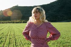 a woman standing in a field with her hands on her hips and looking at the camera