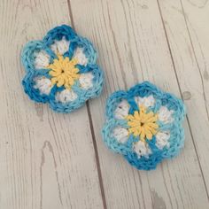 two crocheted flowers sitting on top of a white wooden table next to each other