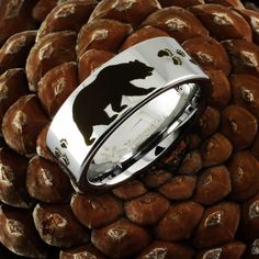 a ring with the silhouette of a bear is sitting on top of a pine cone