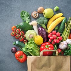 a grocery bag filled with lots of different types of fruits and vegetables on top of a gray surface