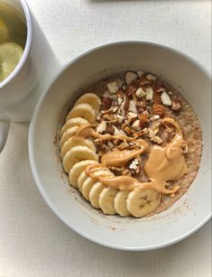 a bowl of oatmeal with bananas and nuts next to a cup of tea