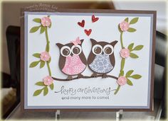 two owls are sitting on a branch with pink flowers and hearts in their beaks