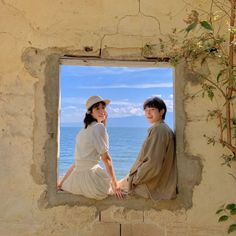 two people are sitting on a window ledge looking out at the water and greenery