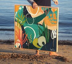 a woman holding up a painting on the beach