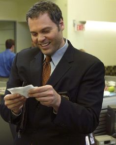 a man in a suit and tie is looking at something on his cell phone while smiling