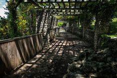 a wooden walkway surrounded by trees and rocks under a pergolated roof in the shade