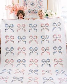 two women holding up a quilt with bows on it