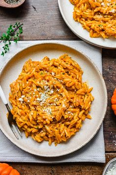 two plates filled with pasta and topped with parmesan sprinkles next to small pumpkins