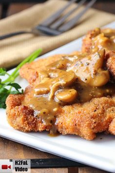 fried chicken with mushroom gravy on a white plate next to greens and a fork