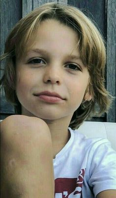 a young boy sitting in front of a wooden fence with his hand on his knees