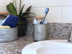 two tin cans with toothbrushes in them sitting on a bathroom counter