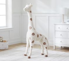 a stuffed giraffe standing on top of a white rug in a child's room