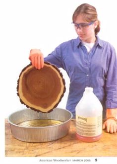 a woman holding a wooden slice over a metal pan with liquid in it on a table