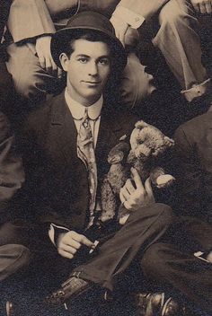 an old black and white photo of a man in a suit holding a teddy bear